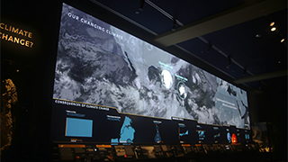A photograph of a large digital screen display showing infrared cloud data