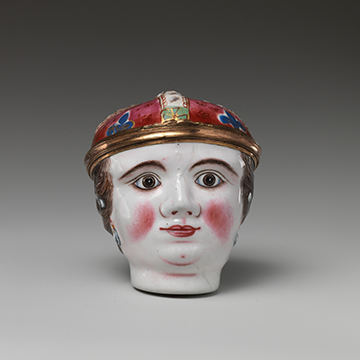 A enamel-painted copper sculpture of a white face with red blushed cheeks and decorative hat