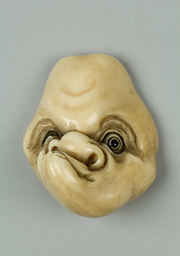 A small sculpture of a mask with a man's lopsided face